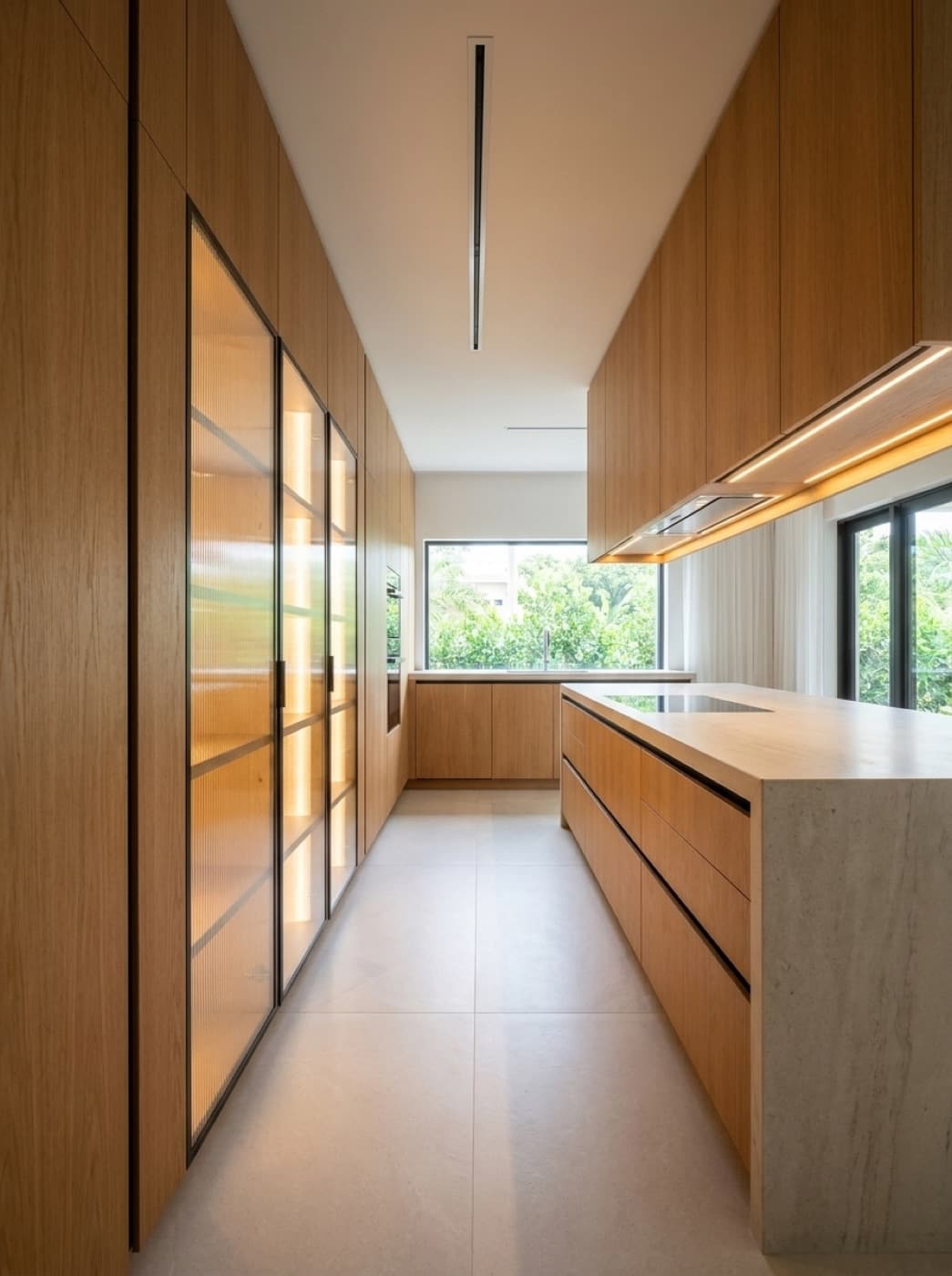 Kitchen with full-height oak cabinetry, aluminum-framed reeded glass doors lit from within and a stone waterfall island