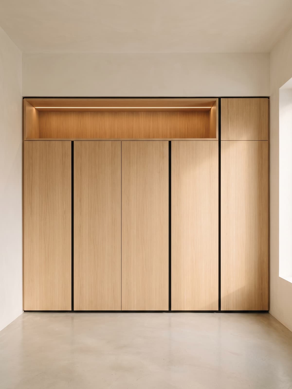 Concept visualization: floor-to-ceiling built-in oak millwork with flush handleless fronts, black shadow-gap reveals and a warm LED strip in the upper recess